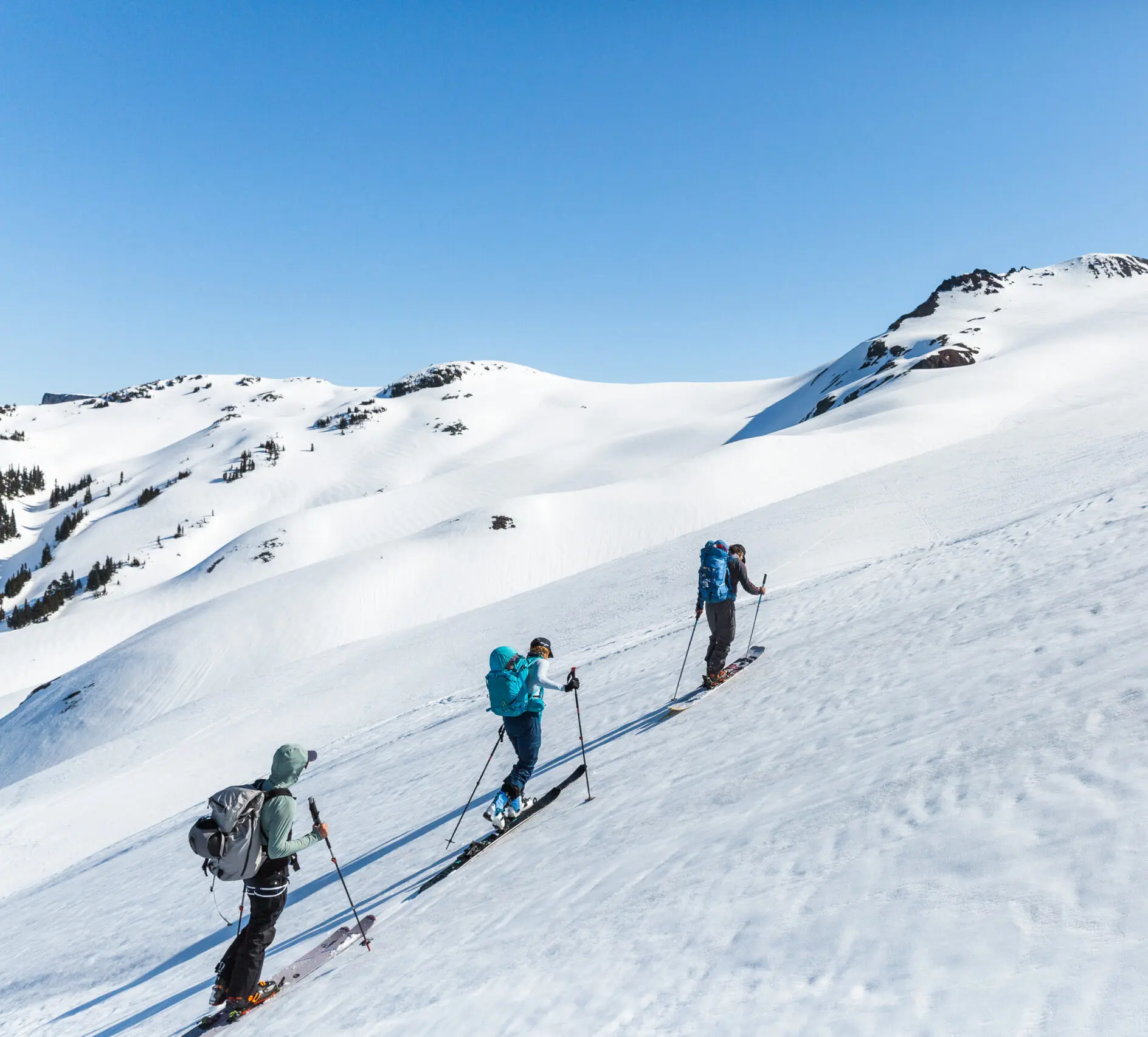 3 skiers ascend a snow covered slope in a line