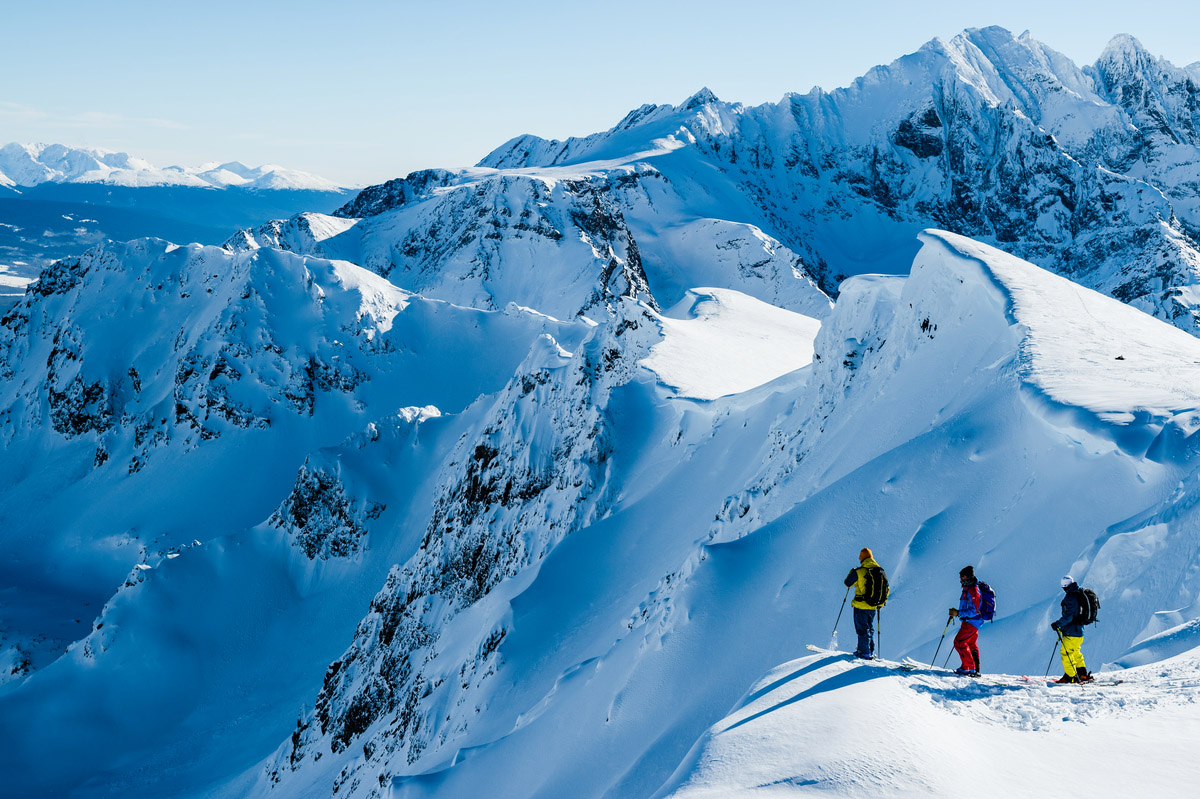 three skiers on top of a mountain peak surrounded by snow and mountains